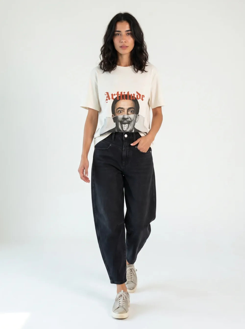 Cream tee with a monochrome portrait print, black barrel-leg jeans, tan sneakers, caught mid-stride