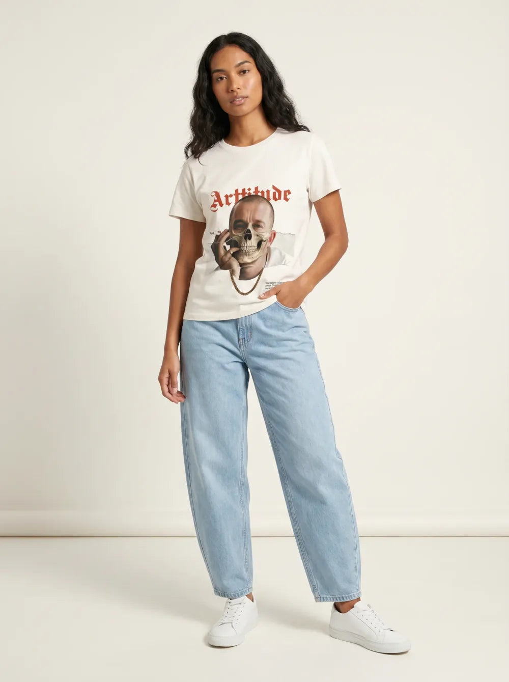 Cream tee with a portrait print, skull graphic over the lower face, light-wash jeans, white sneakers