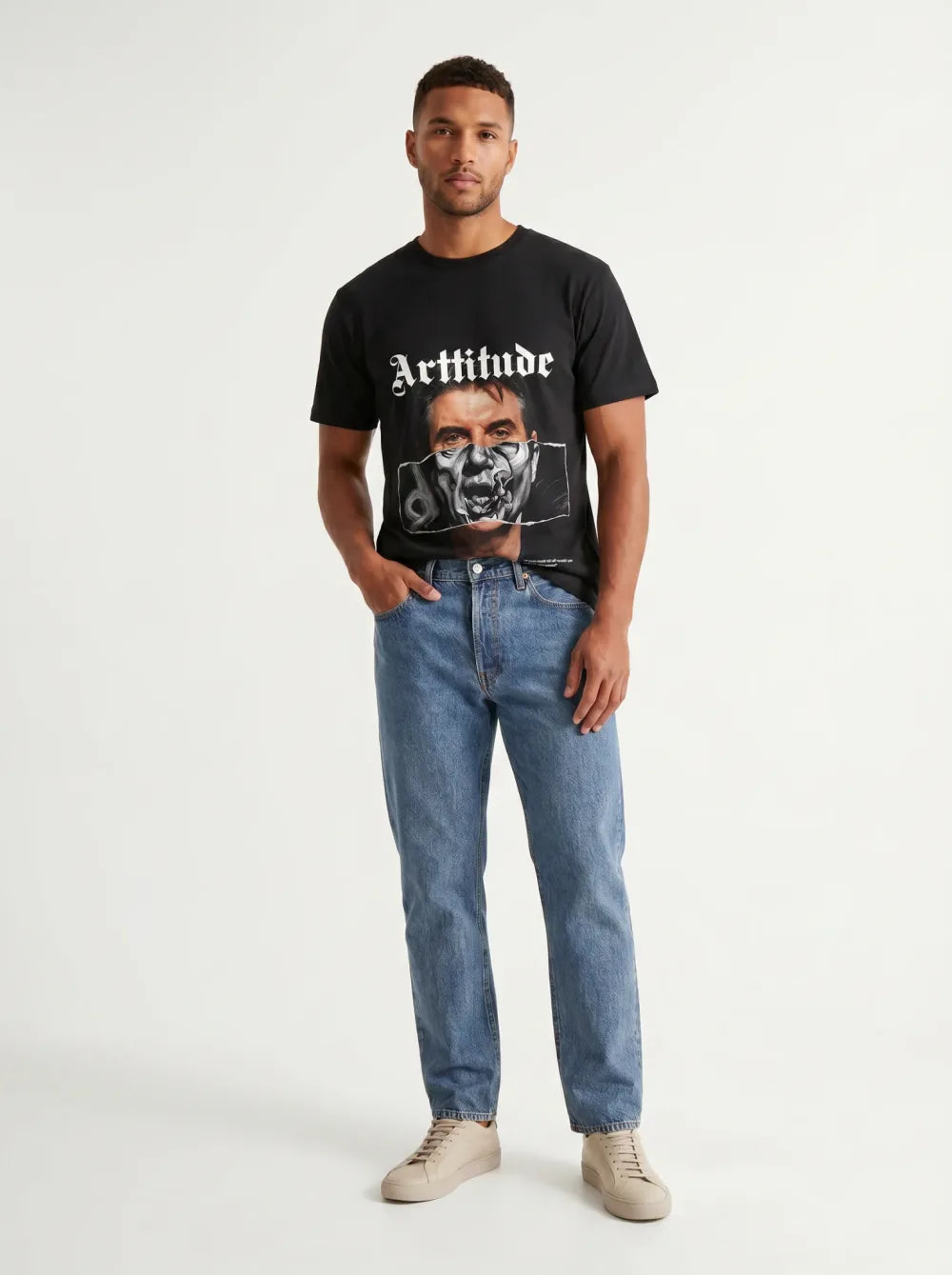 Black tee with a monochrome portrait print, metallic mask over the mouth, mid-wash jeans, tan sneakers
